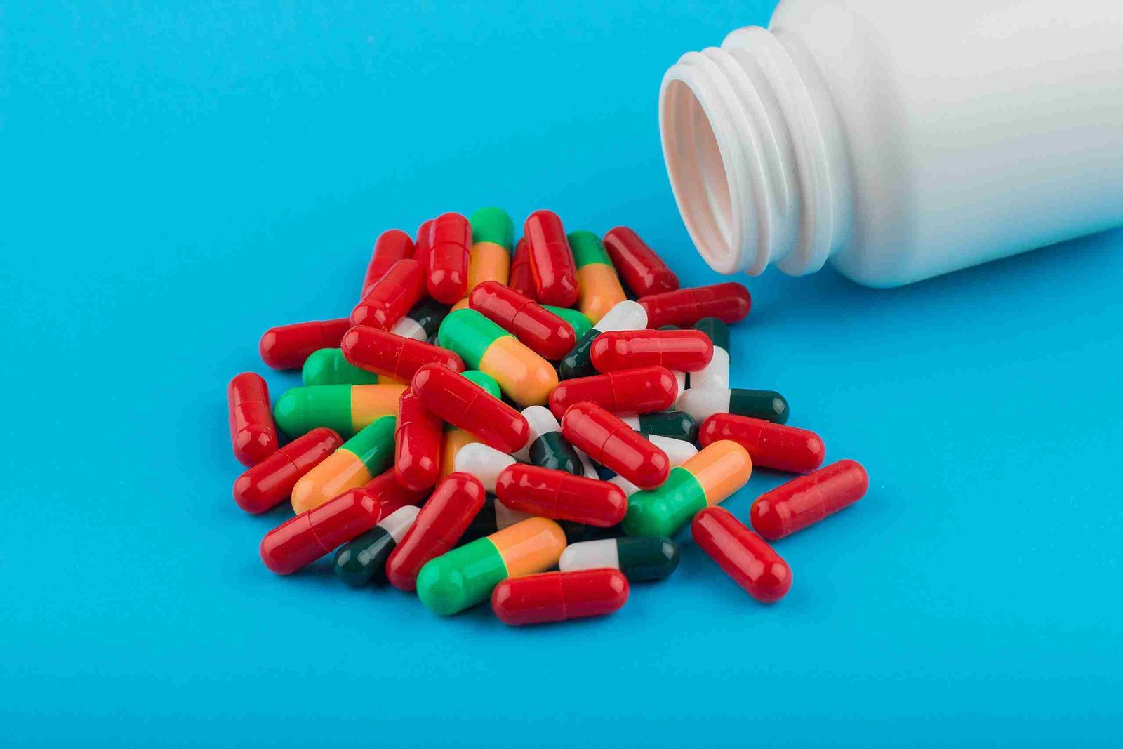 A heap of mixed colored pills with container on a blue background
